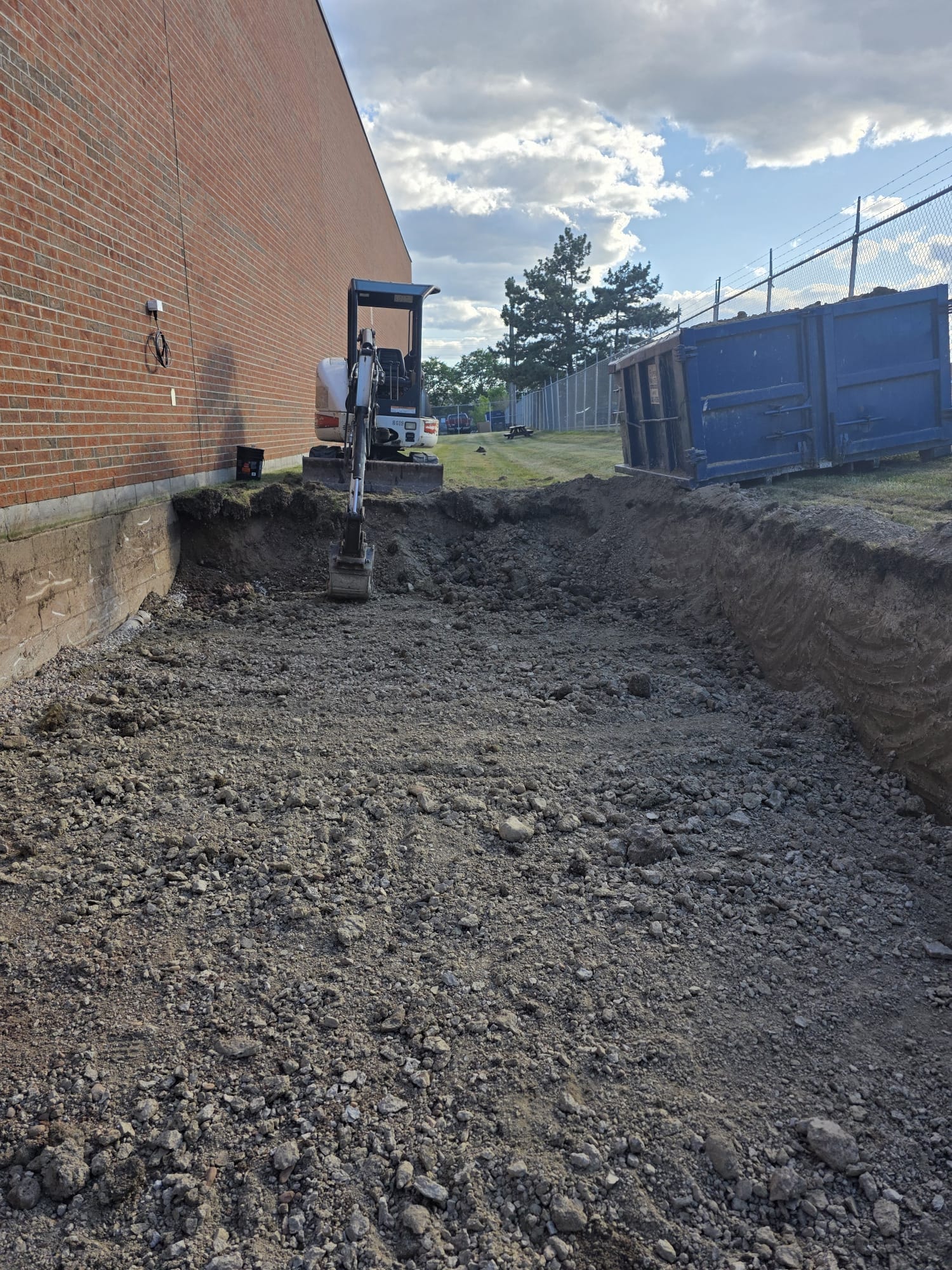 Foundation Excavation — Bobcat Trenching Along Commercial Building