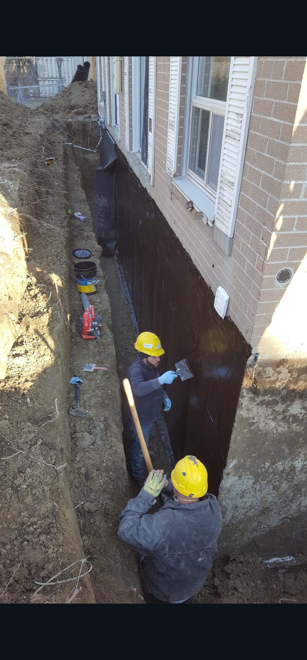 Foundation Waterproofing — Two Workers in Hard Hats Applying Membrane